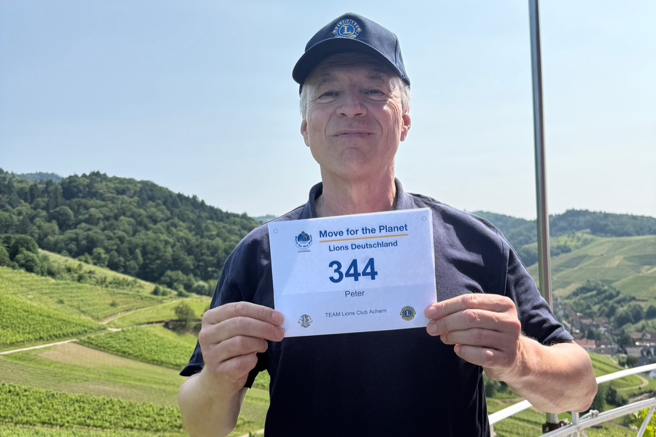 Peter hält seine Move CLASSIC Startnummer 344 bei einer Wanderung durch die grünen Weinberge in die Kamera.