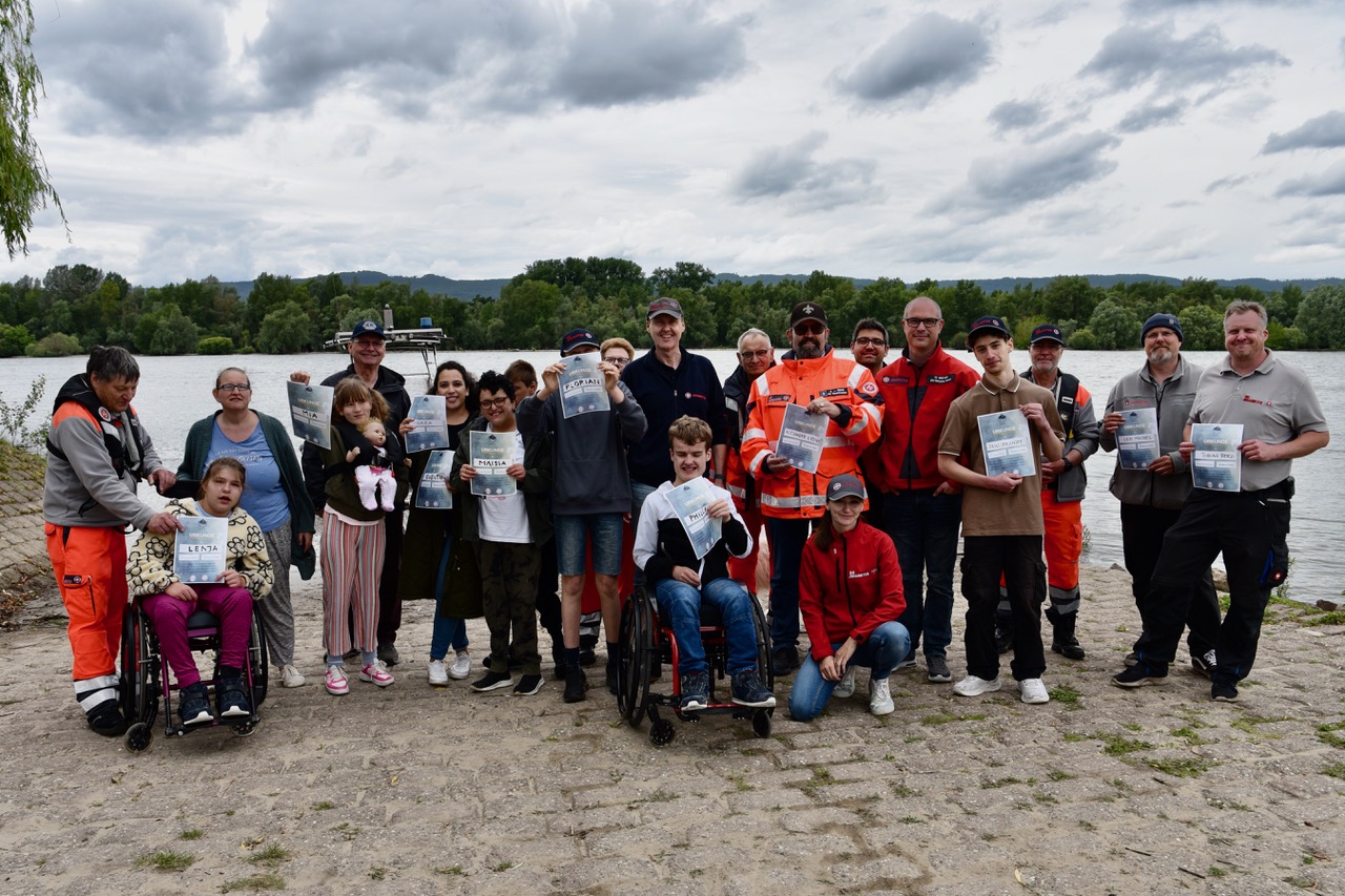 Gruppenbild mit den teilnehmenden junge Rolli-Fahrerinnen und -Fahrer sowie allen Helfer_innen und Betreuer_innen. Viele halten stolz die Teilnahmeurkunden hoch.