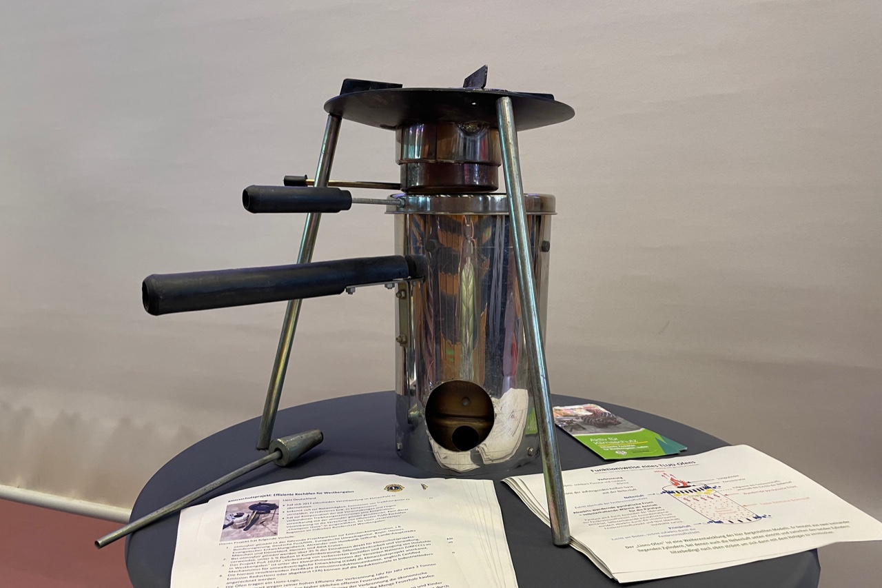 Präsentation des Metallgestells über einen zylindrischen Hohlkörper, der als Brennkammer für Holz dient, während einer Versammlung.