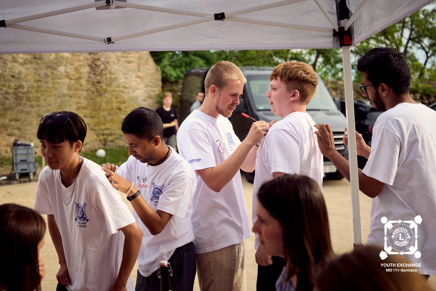 Gruppe Jugendlicher mit weißen T-Shirts die sich gegenseitig positive Nachrichten auf die Shirts schreiben.